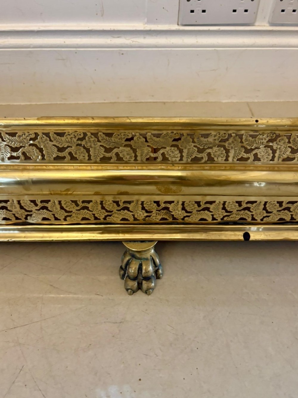 An antique Regency period brass fireplace fender featuring intricate pierced metalwork, claw feet, and matching original brass fire irons positioned at either end. View V