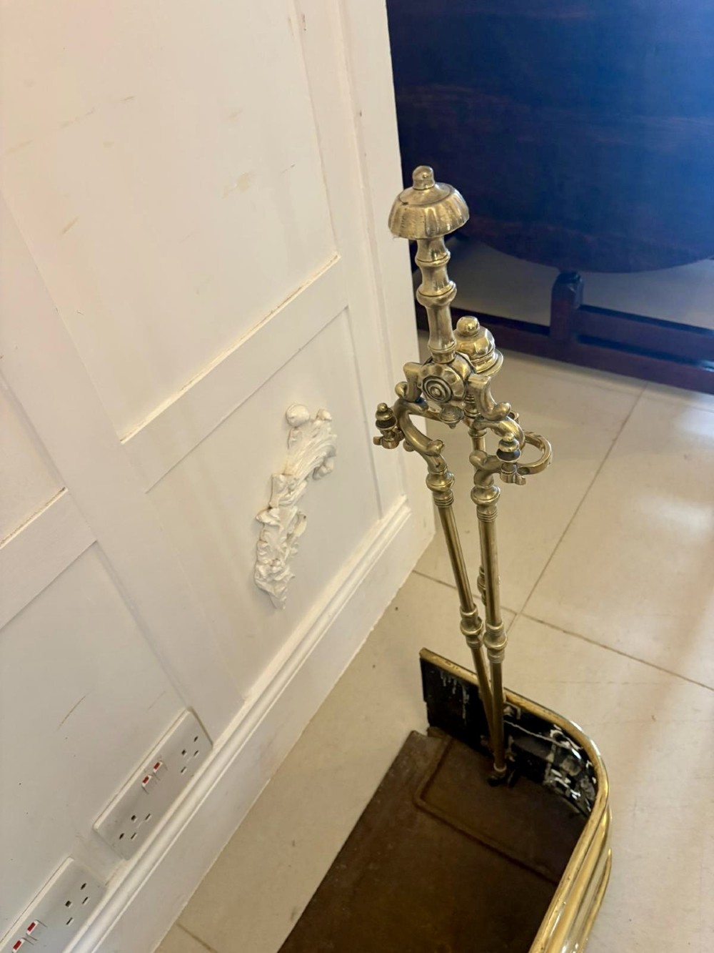 An antique Regency period brass fireplace fender featuring intricate pierced metalwork, claw feet, and matching original brass fire irons positioned at either end. View VI