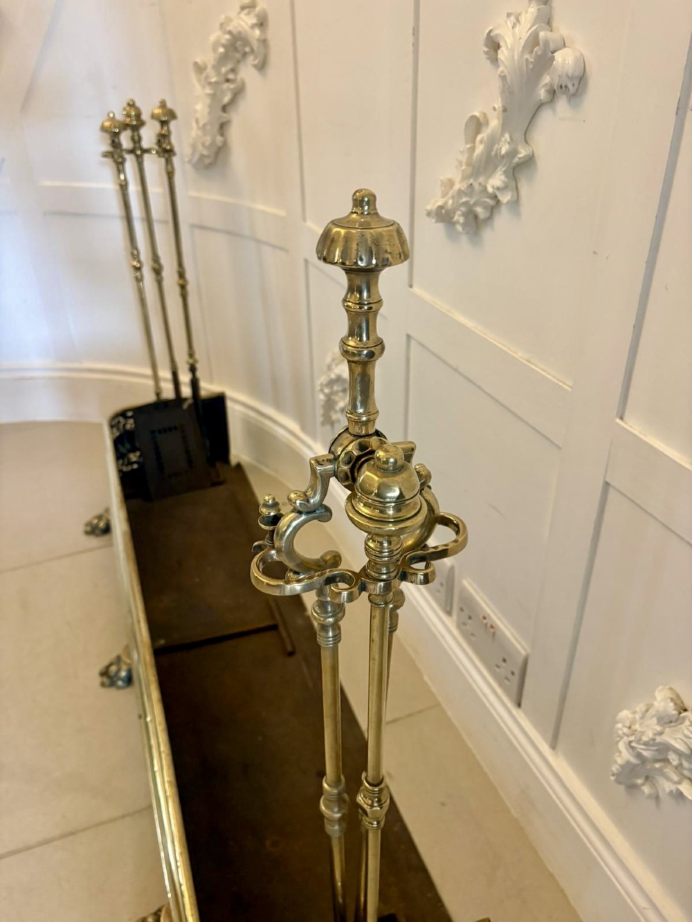 An antique Regency period brass fireplace fender featuring intricate pierced metalwork, claw feet, and matching original brass fire irons positioned at either end. View VII