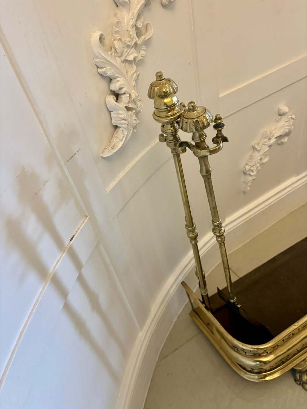 An antique Regency period brass fireplace fender featuring intricate pierced metalwork, claw feet, and matching original brass fire irons positioned at either end. View X