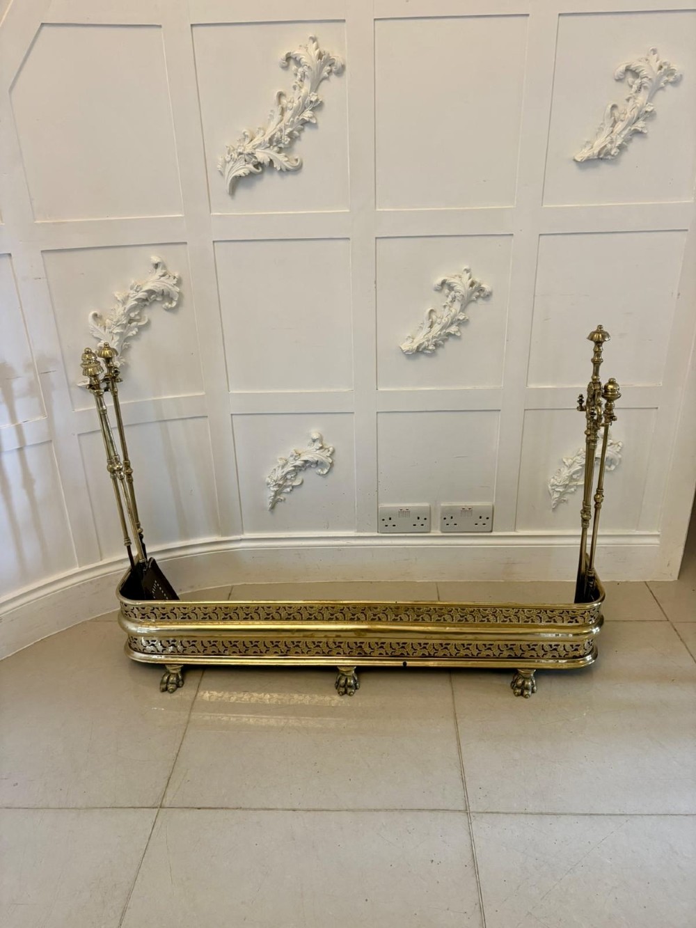 An antique Regency period brass fireplace fender featuring intricate pierced metalwork, claw feet, and matching original brass fire irons positioned at either end. View XII