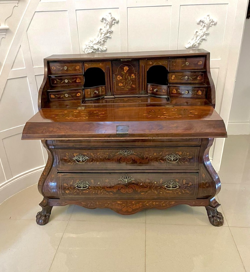 An 18th-century burr walnut bombe bureau featuring floral marquetry inlay, three curved drawers with brass handles, a slant top, and carved feet. View V