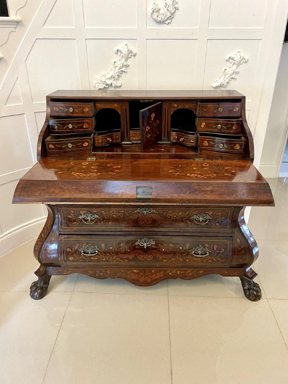 An 18th-century burr walnut bombe bureau featuring floral marquetry inlay, three curved drawers with brass handles, a slant top, and carved feet. View VI