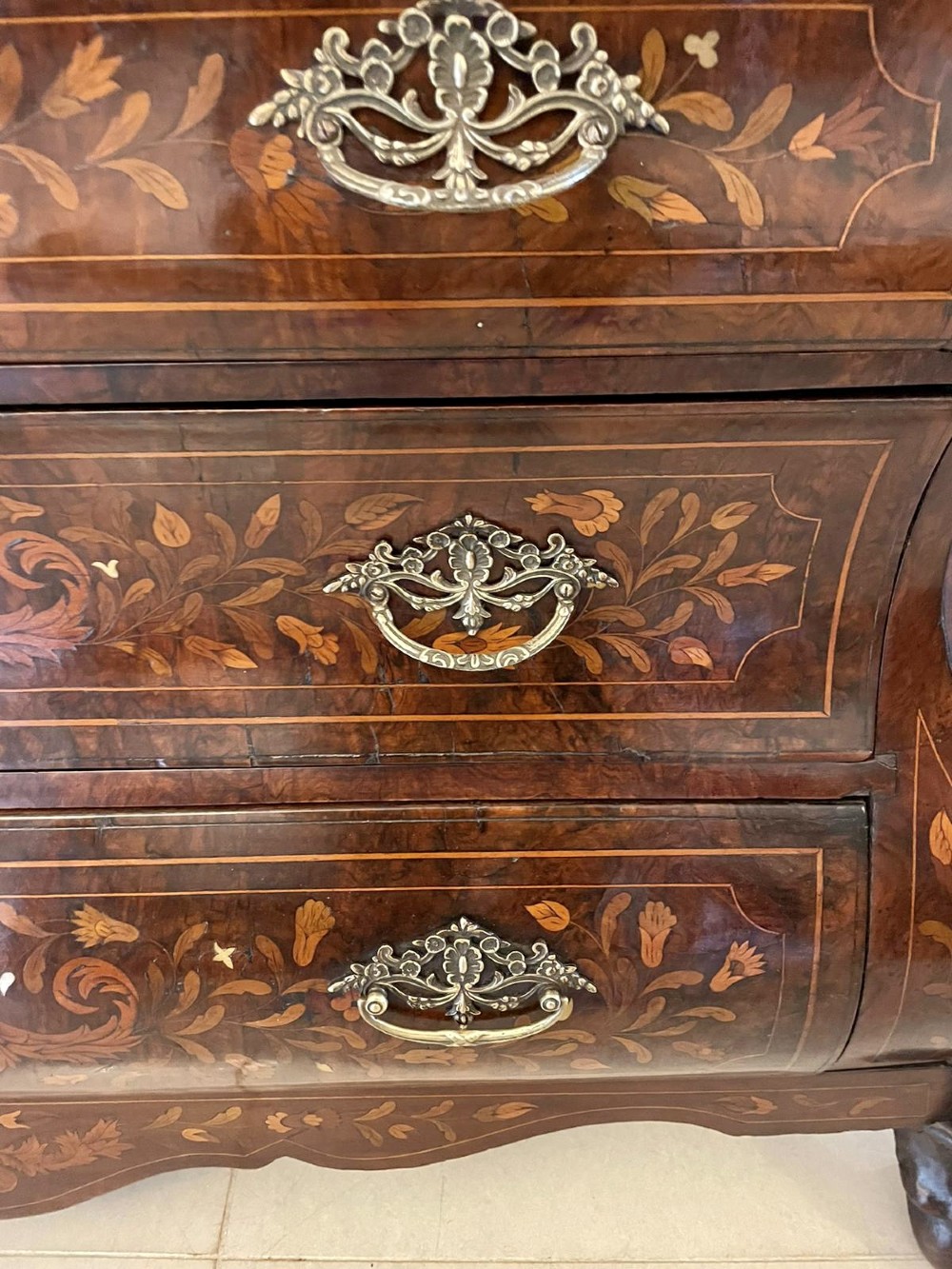 An 18th-century burr walnut bombe bureau featuring floral marquetry inlay, three curved drawers with brass handles, a slant top, and carved feet. View IX