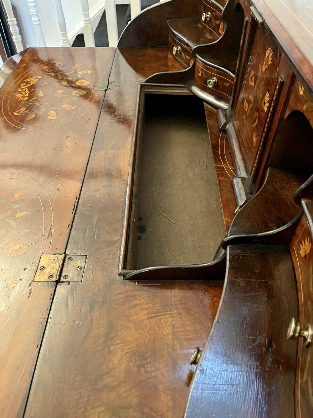 An 18th-century burr walnut bombe bureau featuring floral marquetry inlay, three curved drawers with brass handles, a slant top, and carved feet. View X