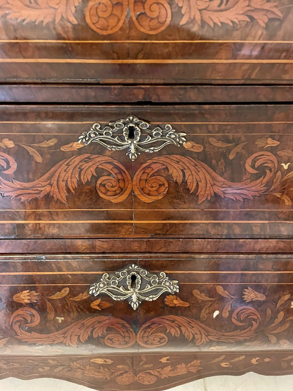 An 18th-century burr walnut bombe bureau featuring floral marquetry inlay, three curved drawers with brass handles, a slant top, and carved feet. View XII
