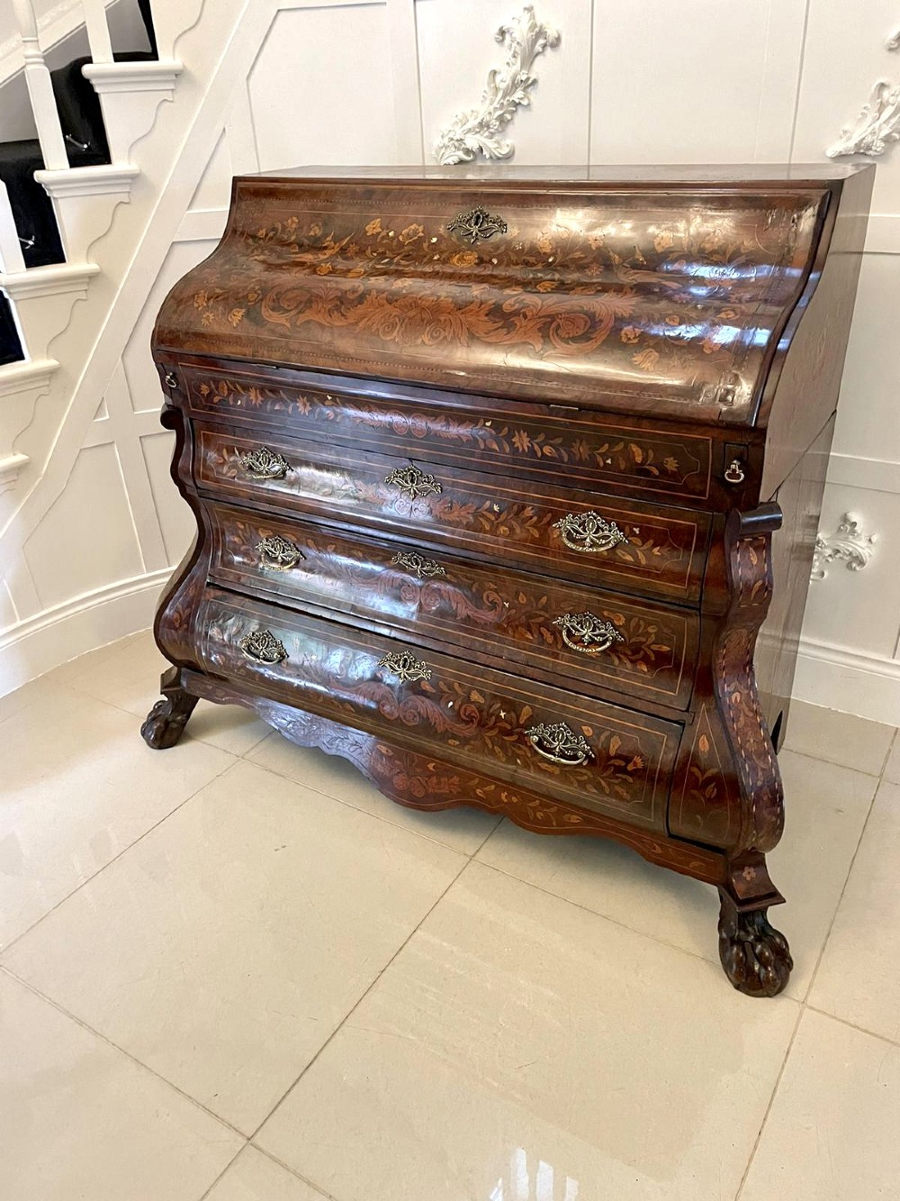 An 18th-century burr walnut bombe bureau featuring floral marquetry inlay, three curved drawers with brass handles, a slant top, and carved feet. View XIV