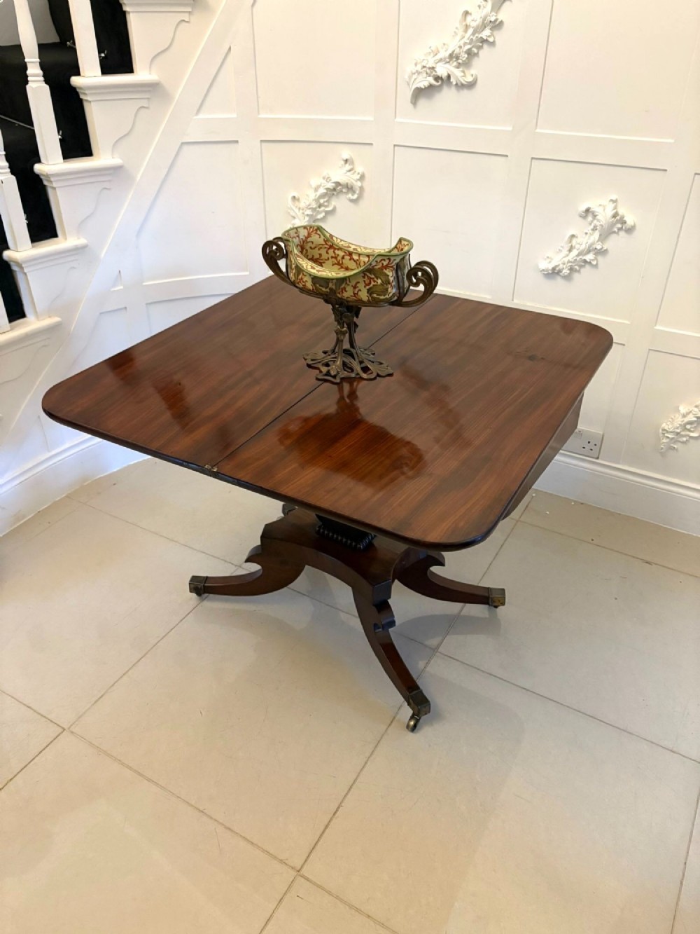 A Regency figured mahogany tea table with a fold-over rectangular top, central pedestal support, and four curved splayed legs on brass castors. View III