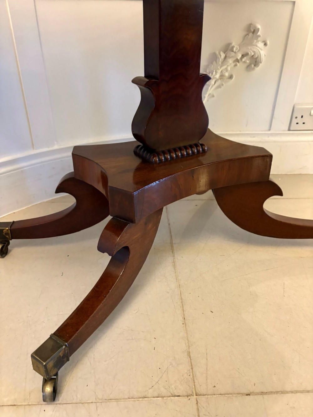 A Regency figured mahogany tea table with a fold-over rectangular top, central pedestal support, and four curved splayed legs on brass castors. View V