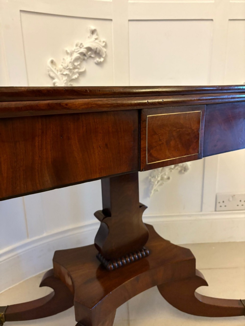 A Regency figured mahogany tea table with a fold-over rectangular top, central pedestal support, and four curved splayed legs on brass castors. View VI