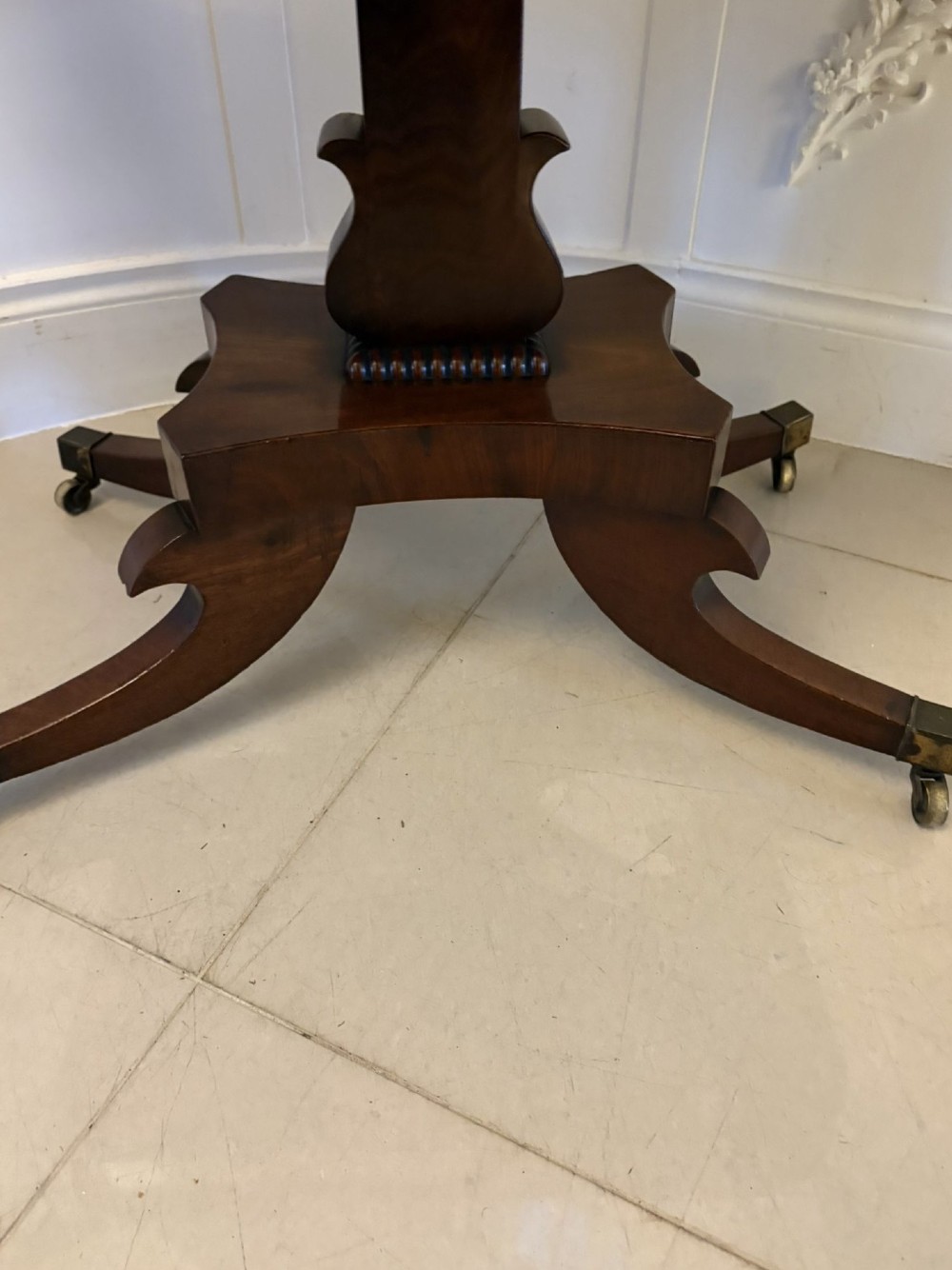 A Regency figured mahogany tea table with a fold-over rectangular top, central pedestal support, and four curved splayed legs on brass castors. View VIII