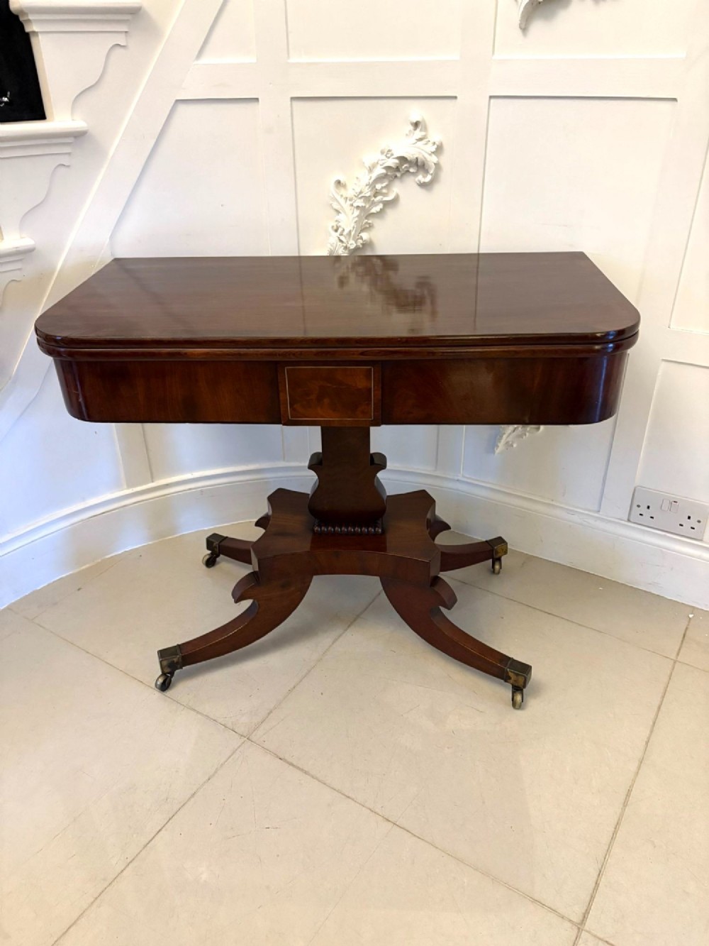 A Regency figured mahogany tea table with a fold-over rectangular top, central pedestal support, and four curved splayed legs on brass castors.