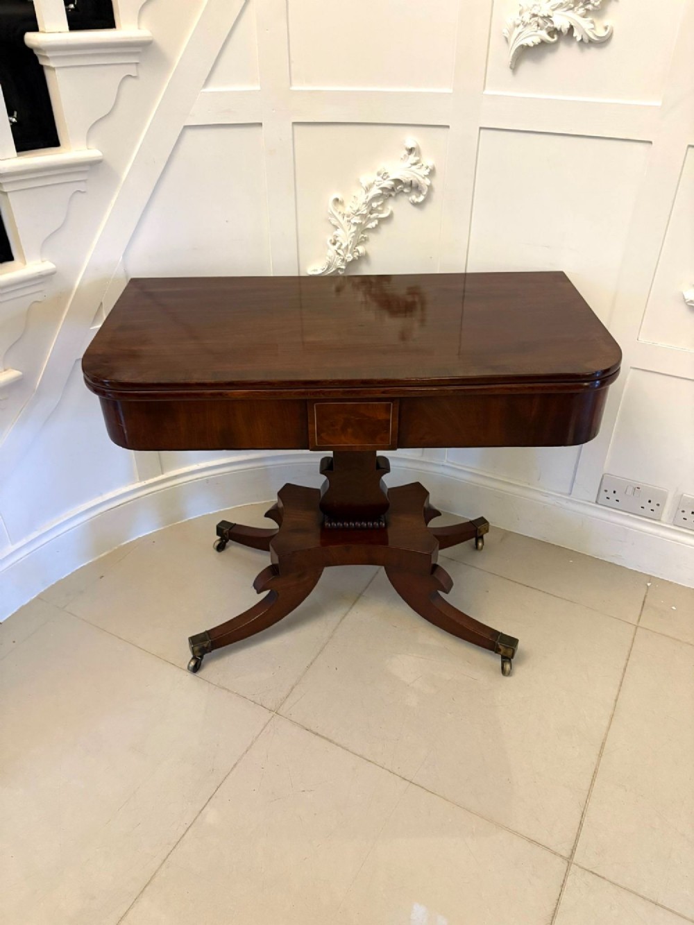 A Regency figured mahogany tea table with a fold-over rectangular top, central pedestal support, and four curved splayed legs on brass castors. View IX
