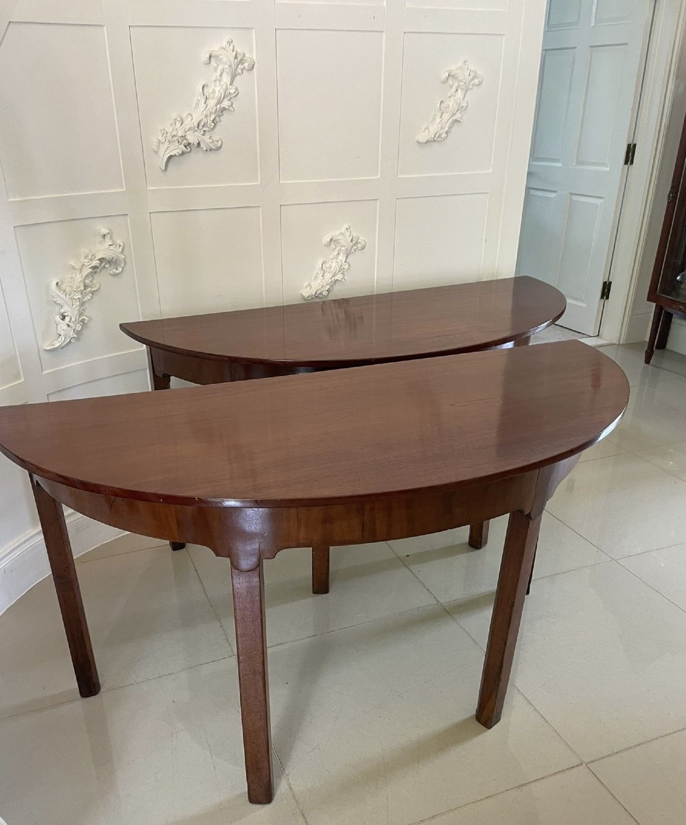 A pair of George III mahogany demi-lune console tables with polished semi-circular tops and straight tapered legs. View X