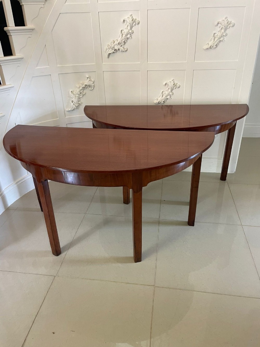 A pair of George III mahogany demi-lune console tables with polished semi-circular tops and straight tapered legs.