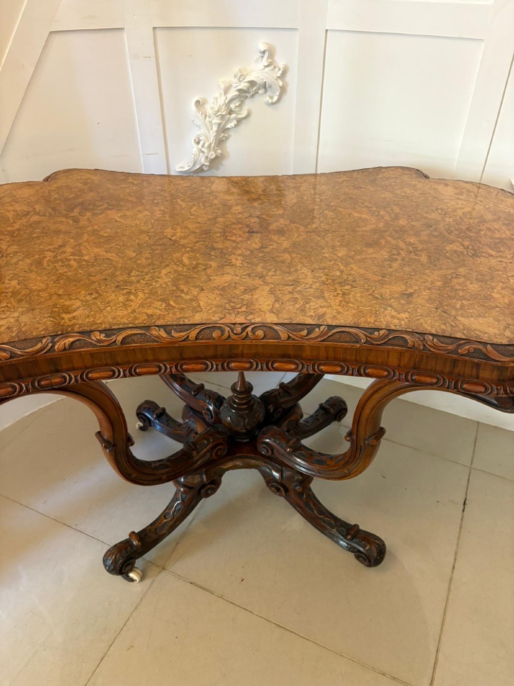 A Victorian burr walnut centre table featuring a shaped top, carved scroll frieze, and an elaborate four-legged base with a central turned finial. View III