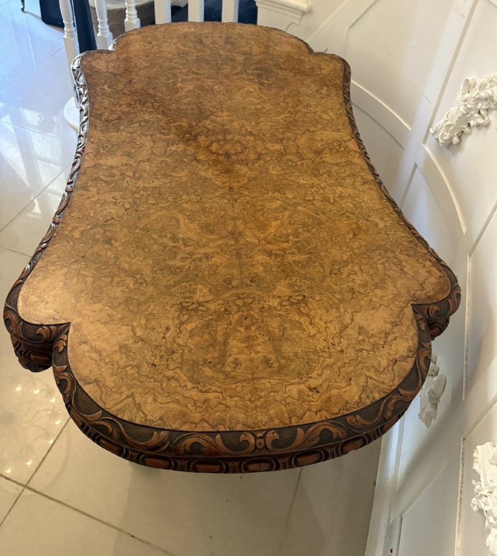 A Victorian burr walnut centre table featuring a shaped top, carved scroll frieze, and an elaborate four-legged base with a central turned finial. View IV