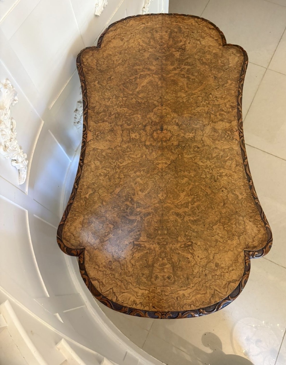 A Victorian burr walnut centre table featuring a shaped top, carved scroll frieze, and an elaborate four-legged base with a central turned finial. View VI