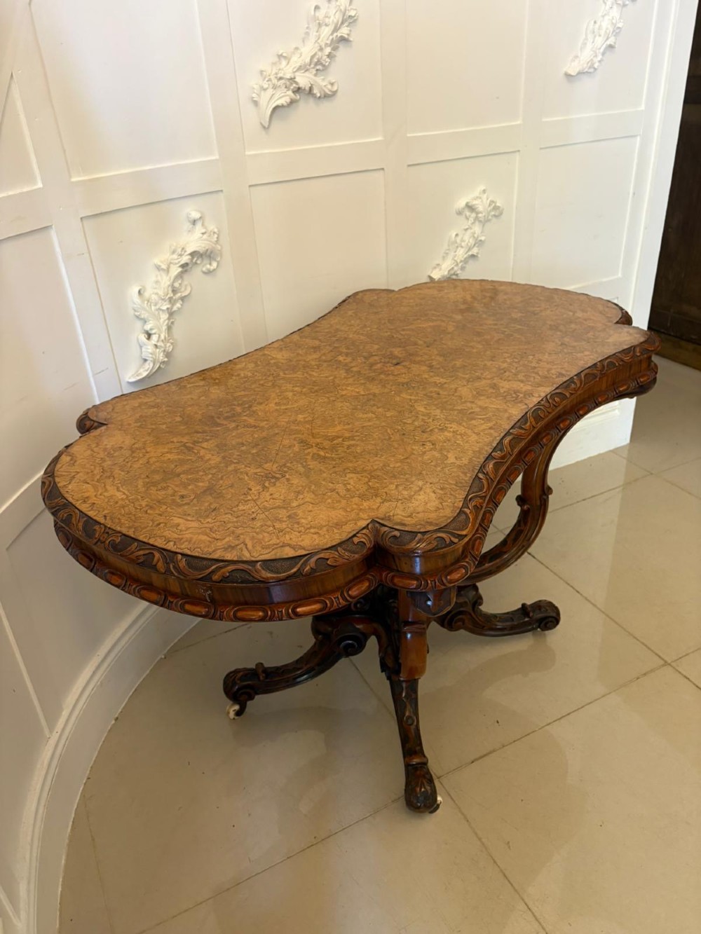 A Victorian burr walnut centre table featuring a shaped top, carved scroll frieze, and an elaborate four-legged base with a central turned finial. View VII