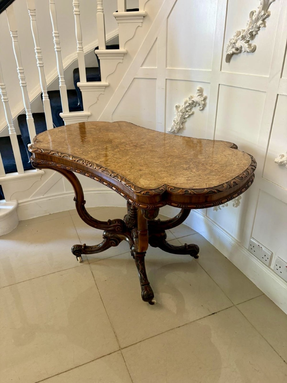 A Victorian burr walnut centre table featuring a shaped top, carved scroll frieze, and an elaborate four-legged base with a central turned finial. View XI