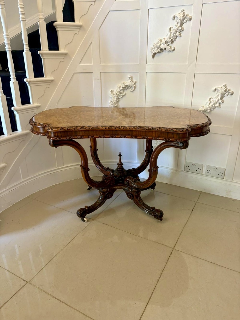A Victorian burr walnut centre table featuring a shaped top, carved scroll frieze, and an elaborate four-legged base with a central turned finial. View XII