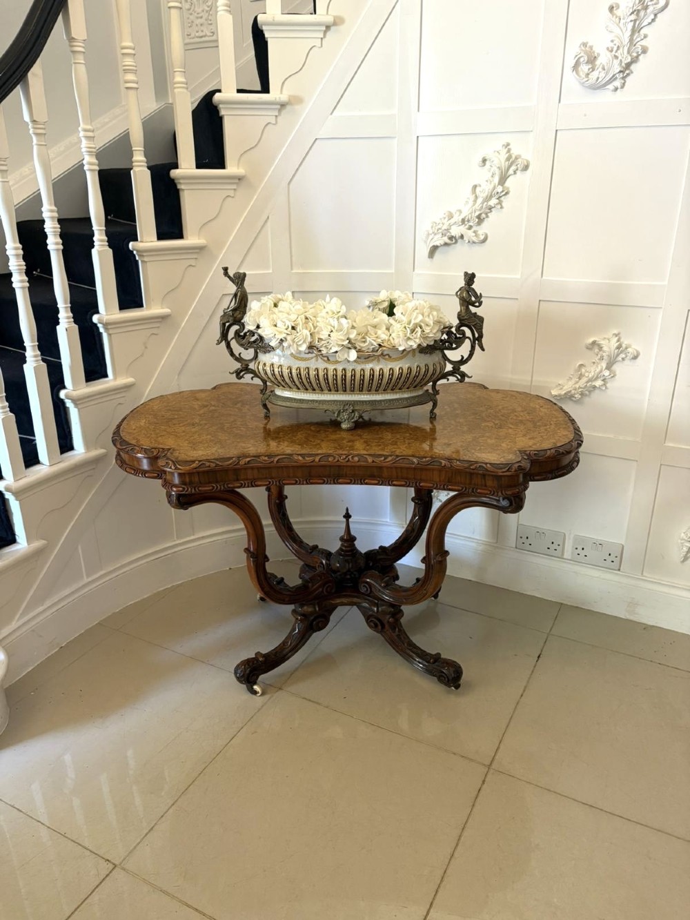 A Victorian burr walnut centre table featuring a shaped top, carved scroll frieze, and an elaborate four-legged base with a central turned finial. View XIII