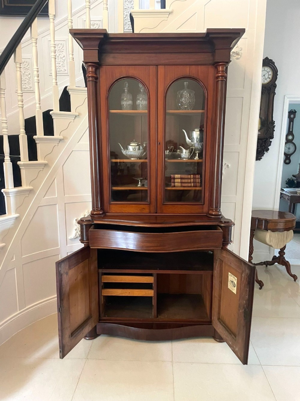 A Victorian mahogany glazed bookcase featuring two upper arched glass doors flanked by turned columns above a curved two-door cupboard base. View V