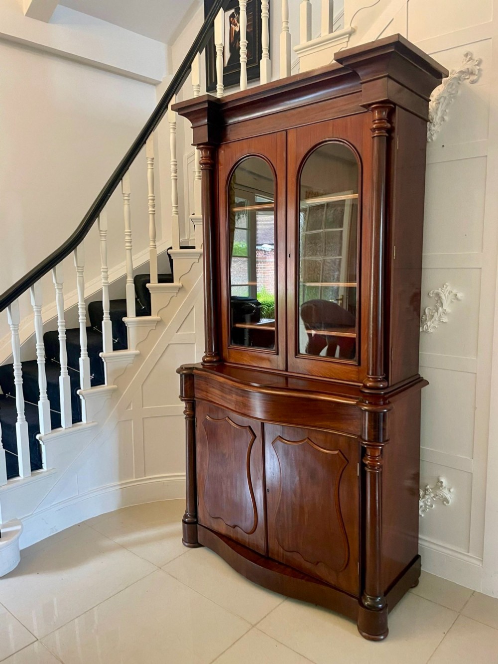 A Victorian mahogany glazed bookcase featuring two upper arched glass doors flanked by turned columns above a curved two-door cupboard base. View VI