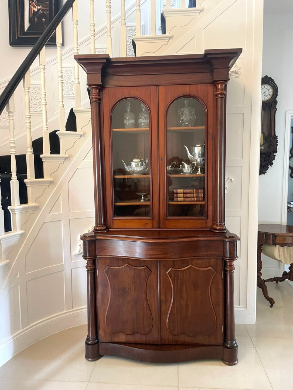 A Victorian mahogany glazed bookcase featuring two upper arched glass doors flanked by turned columns above a curved two-door cupboard base. View XI