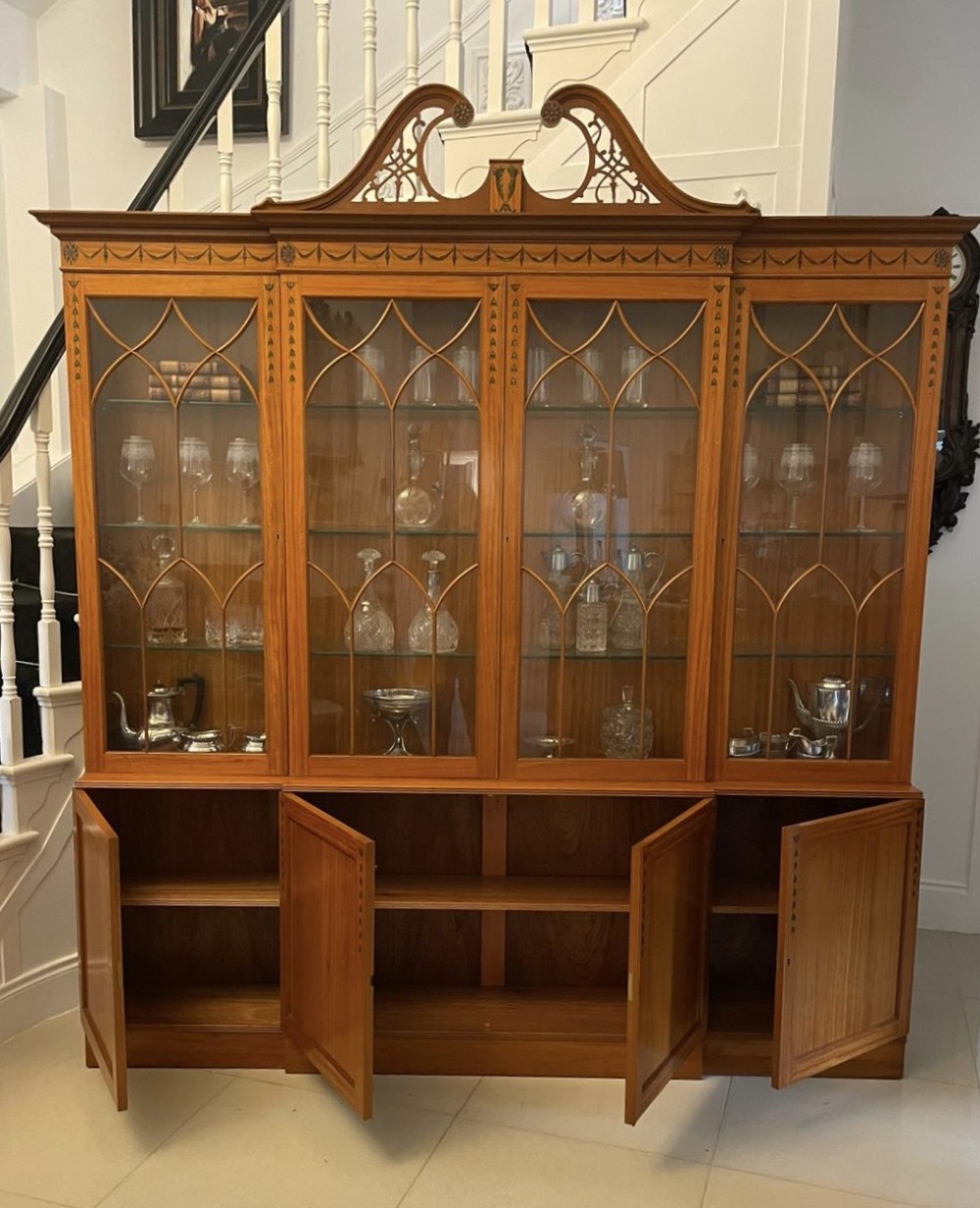 A large satinwood breakfront display cabinet featuring a swan-neck pediment, astragal glazed upper doors, and painted neoclassical motifs. View III