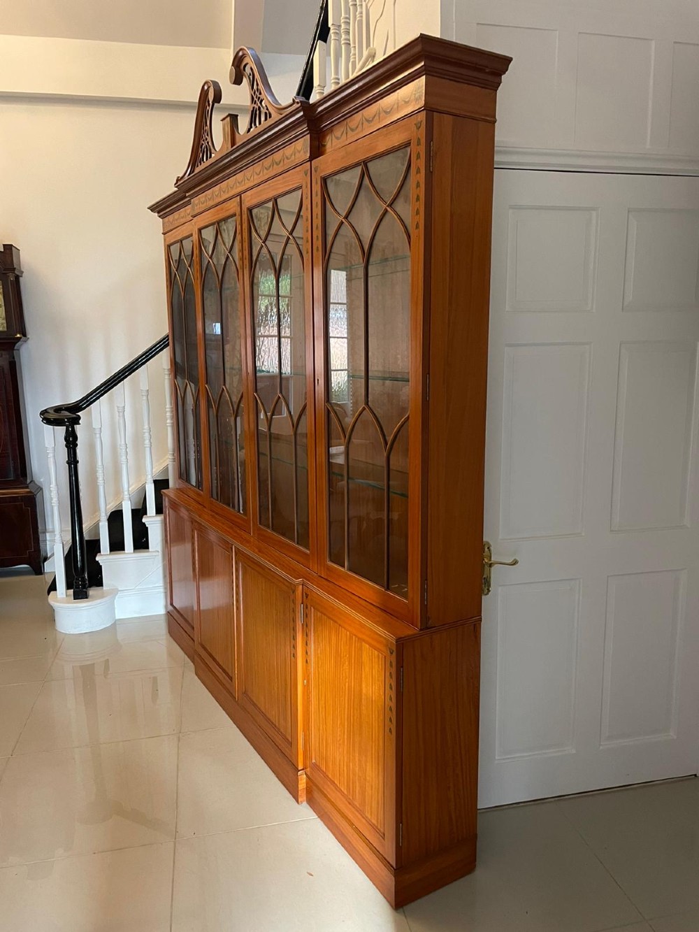 A large satinwood breakfront display cabinet featuring a swan-neck pediment, astragal glazed upper doors, and painted neoclassical motifs. View V