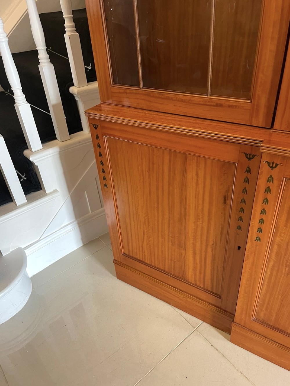 A large satinwood breakfront display cabinet featuring a swan-neck pediment, astragal glazed upper doors, and painted neoclassical motifs. View VIII