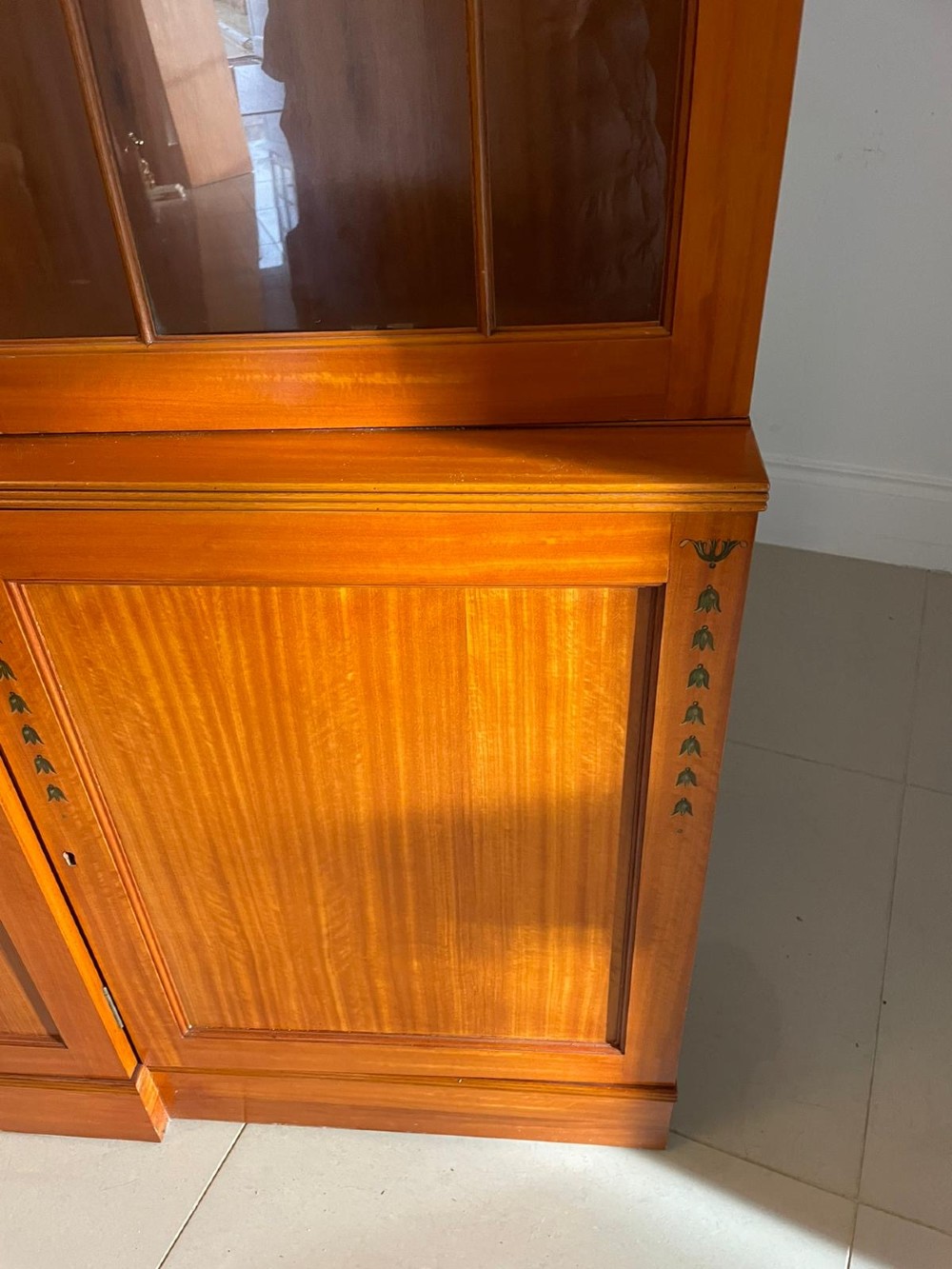 A large satinwood breakfront display cabinet featuring a swan-neck pediment, astragal glazed upper doors, and painted neoclassical motifs. View IX