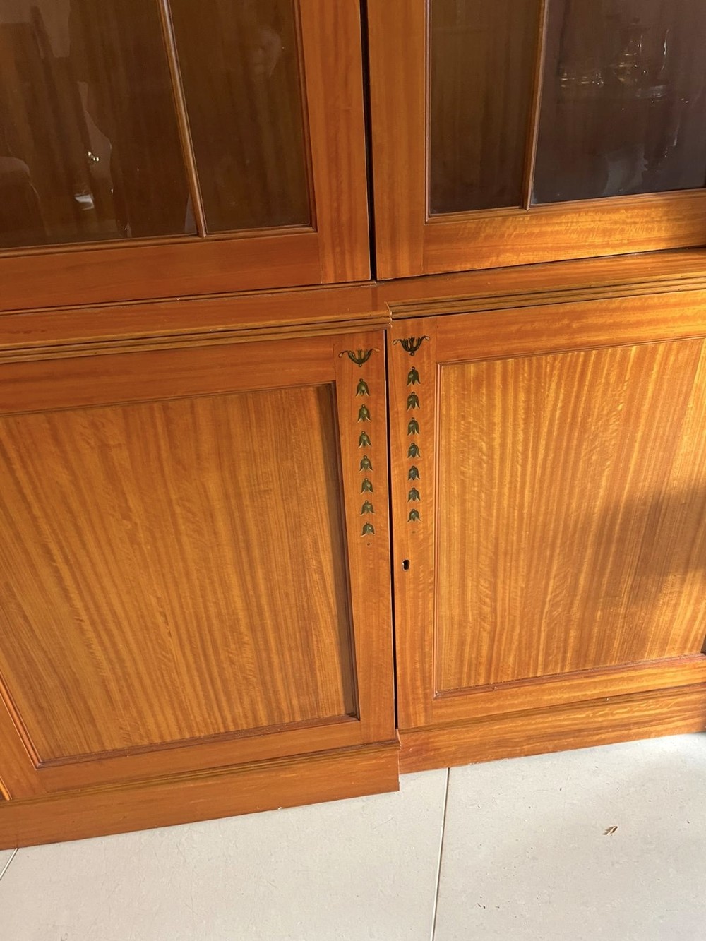 A large satinwood breakfront display cabinet featuring a swan-neck pediment, astragal glazed upper doors, and painted neoclassical motifs. View X