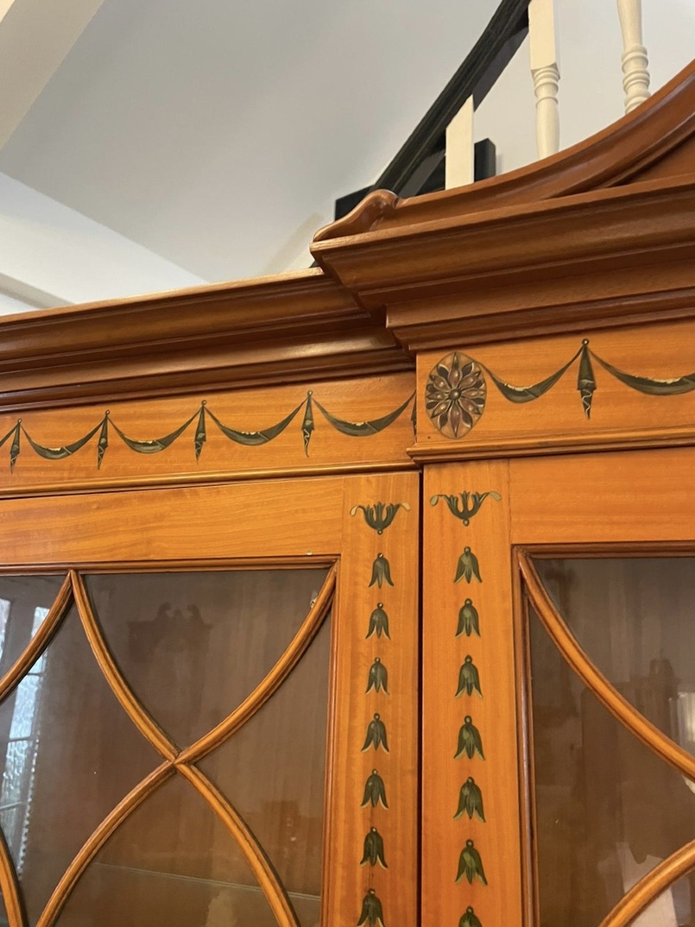 A large satinwood breakfront display cabinet featuring a swan-neck pediment, astragal glazed upper doors, and painted neoclassical motifs. View XII