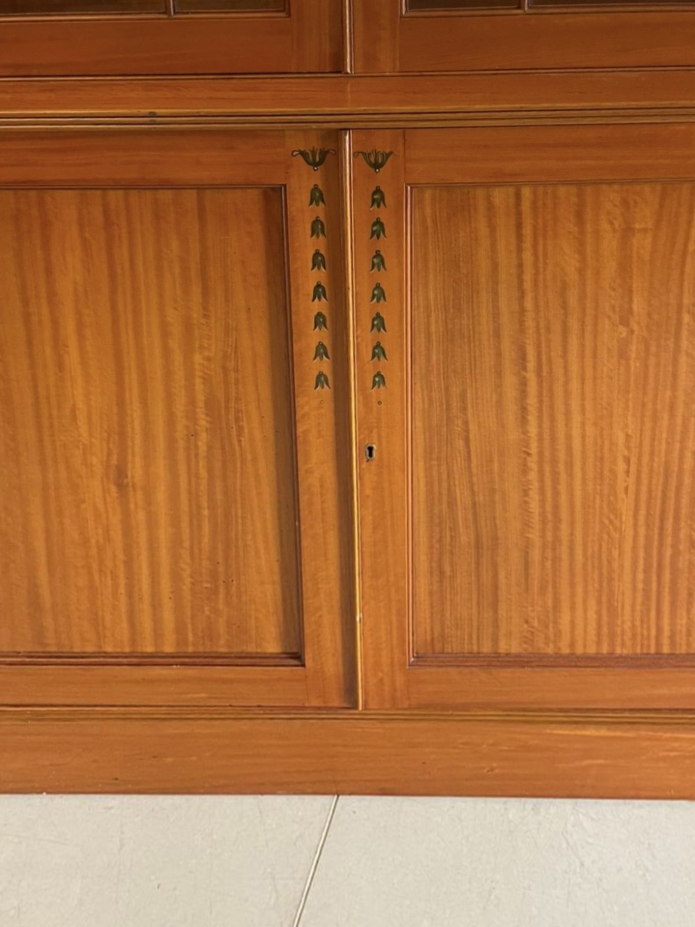 A large satinwood breakfront display cabinet featuring a swan-neck pediment, astragal glazed upper doors, and painted neoclassical motifs. View XIII
