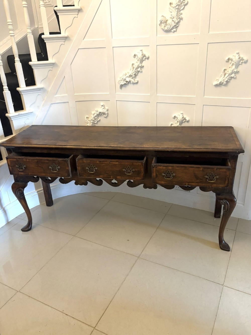 A dark brown oak Georgian style dresser base featuring three drawers with brass drop handles, a decorative scalloped apron, and front cabriole legs. View VIII