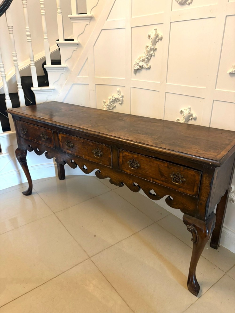 A dark brown oak Georgian style dresser base featuring three drawers with brass drop handles, a decorative scalloped apron, and front cabriole legs. View IX