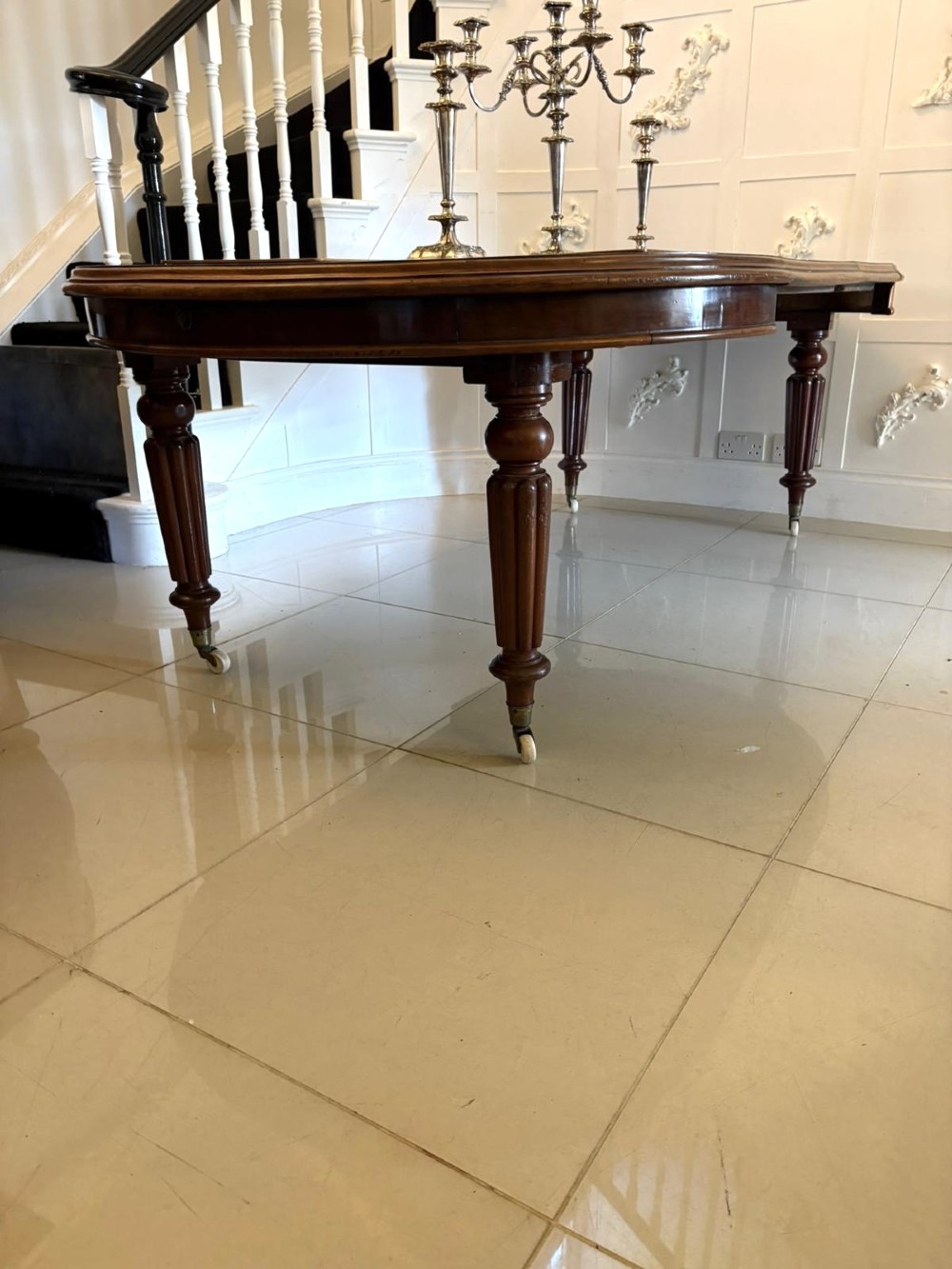 An antique Victorian oval mahogany dining table featuring a wind-out extending mechanism, fluted turned legs, and ceramic castors. View III