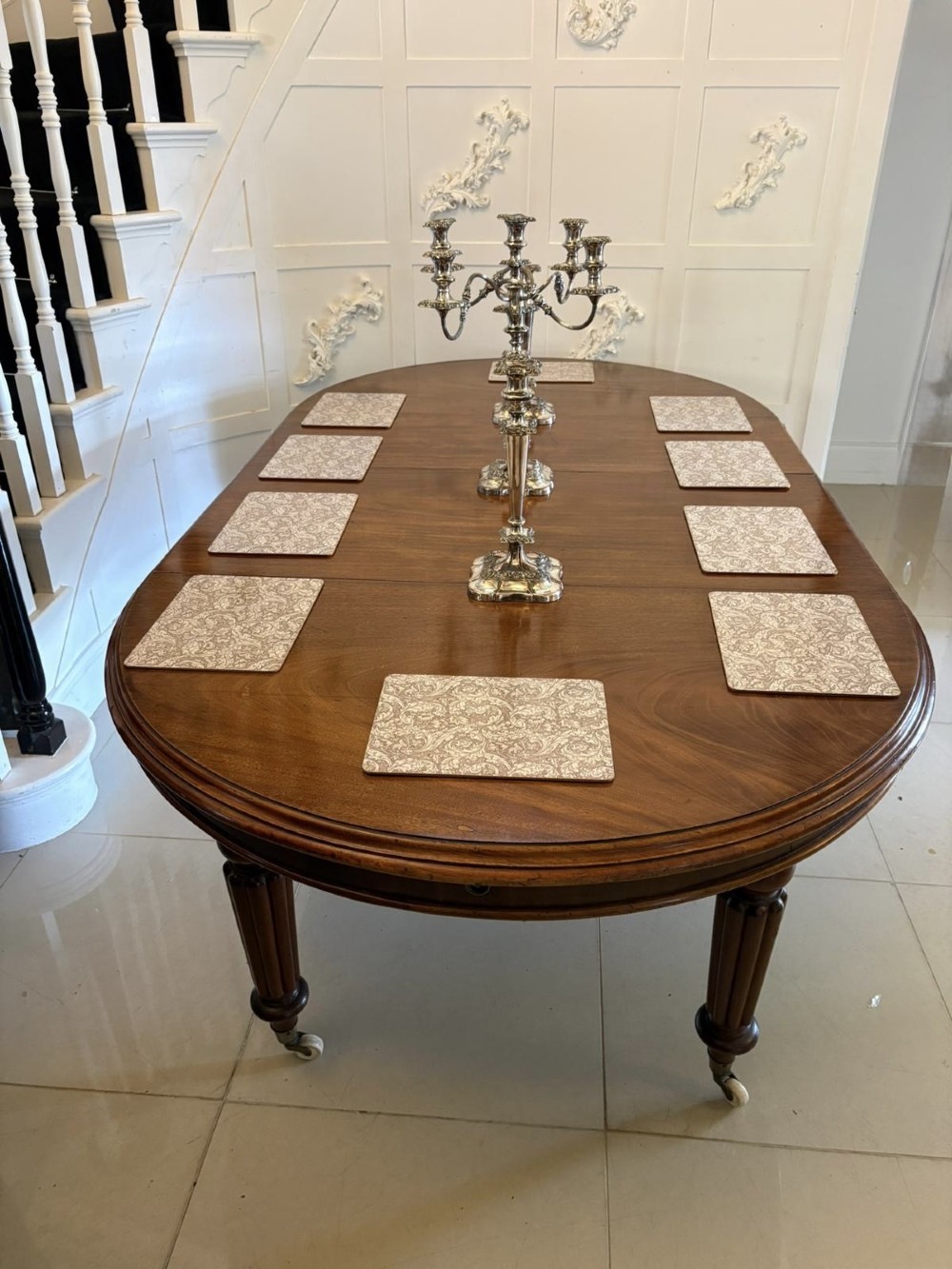 An antique Victorian oval mahogany dining table featuring a wind-out extending mechanism, fluted turned legs, and ceramic castors. View IV