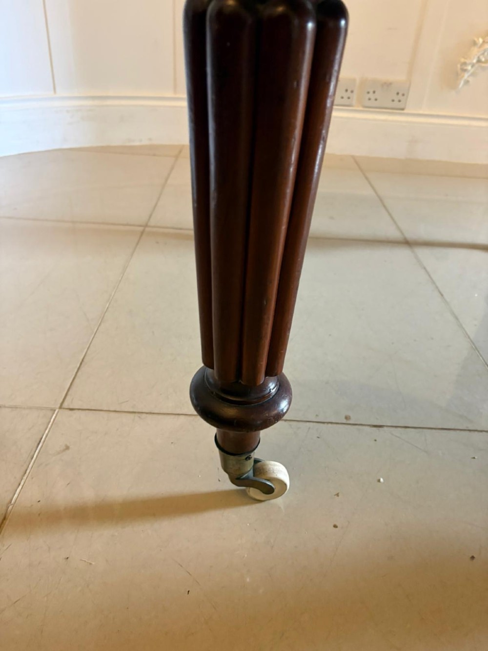 An antique Victorian oval mahogany dining table featuring a wind-out extending mechanism, fluted turned legs, and ceramic castors. View VI