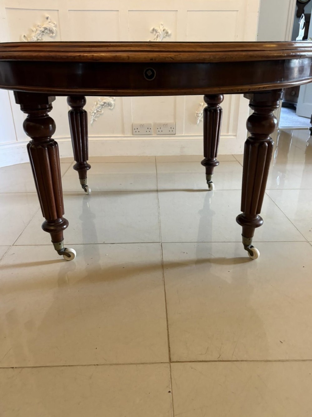 An antique Victorian oval mahogany dining table featuring a wind-out extending mechanism, fluted turned legs, and ceramic castors. View VIII