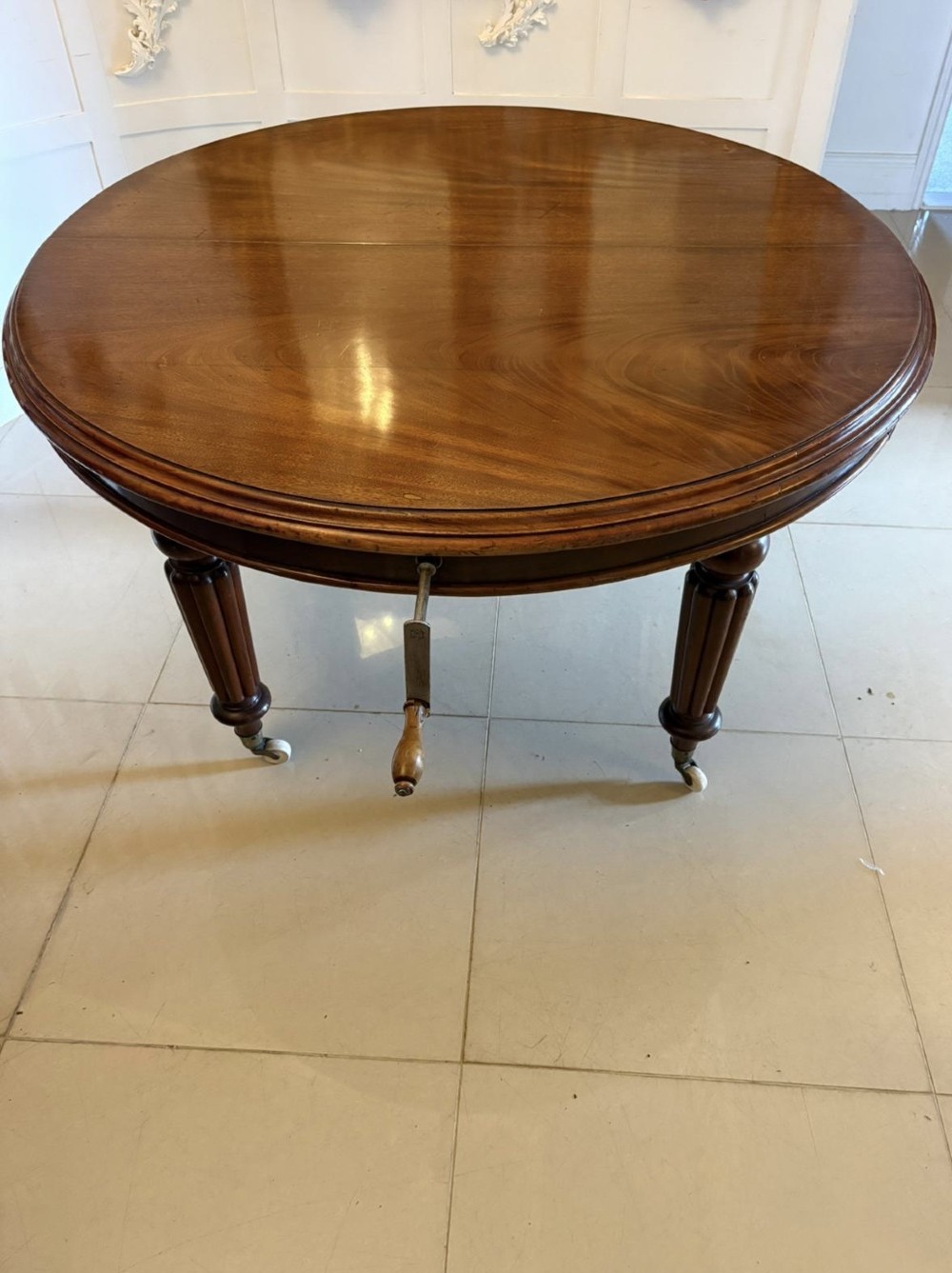 An antique Victorian oval mahogany dining table featuring a wind-out extending mechanism, fluted turned legs, and ceramic castors. View X