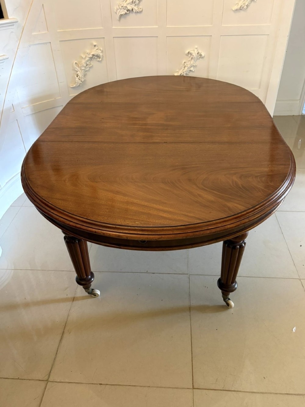 An antique Victorian oval mahogany dining table featuring a wind-out extending mechanism, fluted turned legs, and ceramic castors.