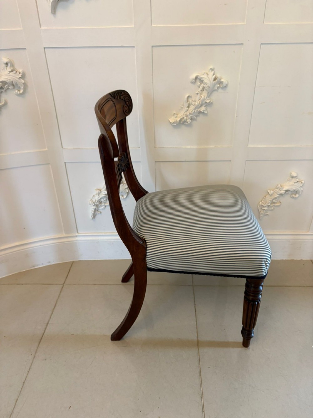 A set of four antique Regency mahogany dining chairs with carved top rails, reeded turned front legs, and blue and white striped upholstered seats. View II