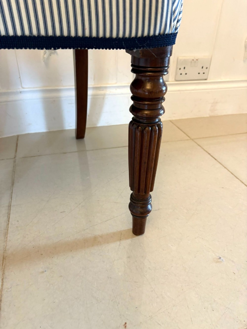 A set of four antique Regency mahogany dining chairs with carved top rails, reeded turned front legs, and blue and white striped upholstered seats. View IV