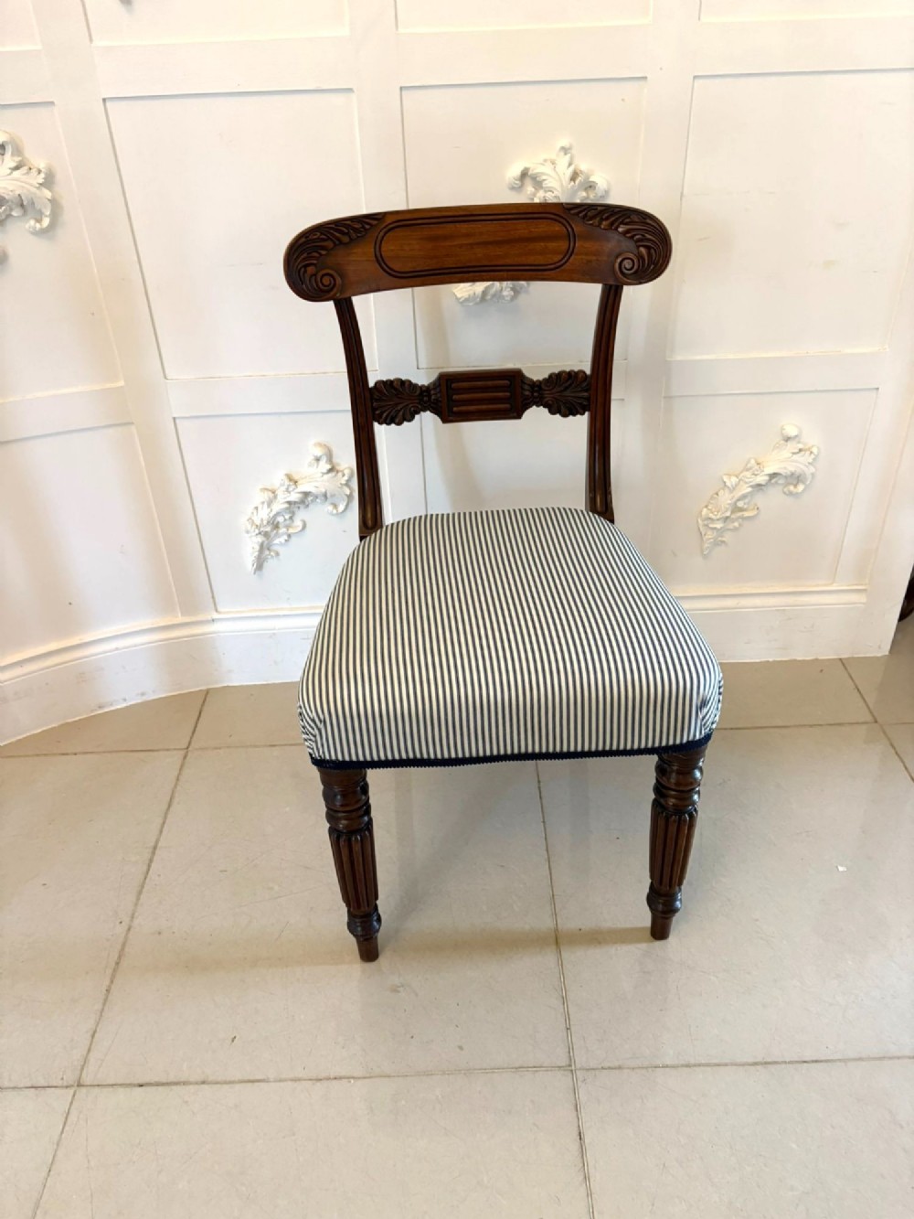 A set of four antique Regency mahogany dining chairs with carved top rails, reeded turned front legs, and blue and white striped upholstered seats. View V