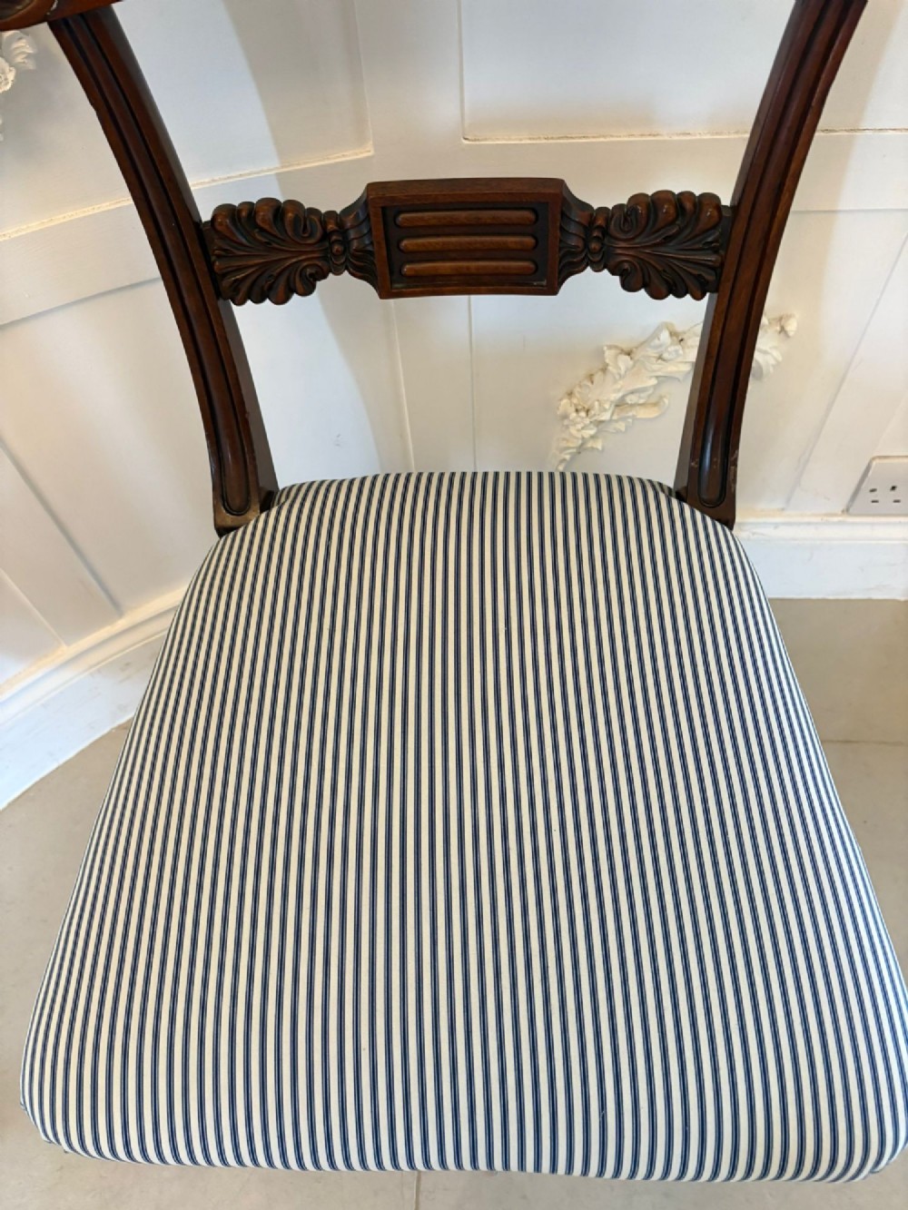 A set of four antique Regency mahogany dining chairs with carved top rails, reeded turned front legs, and blue and white striped upholstered seats. View X