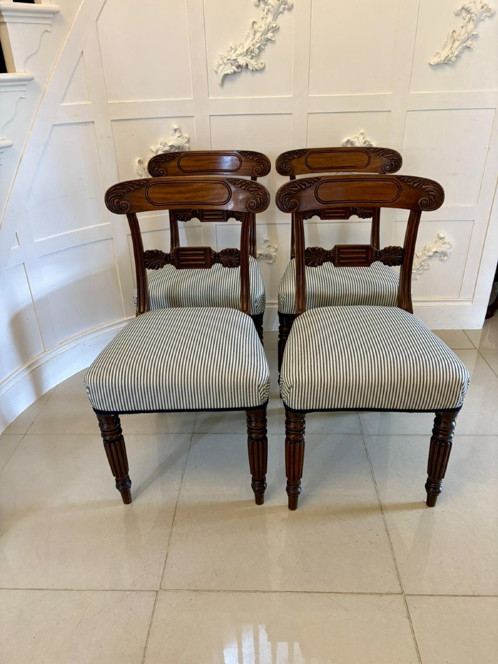 A set of four antique Regency mahogany dining chairs with carved top rails, reeded turned front legs, and blue and white striped upholstered seats. View XIII