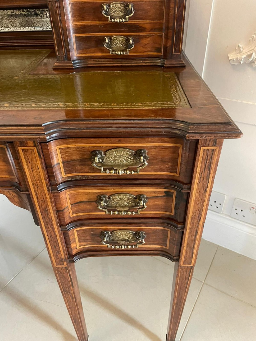 An antique Victorian inlaid writing desk with a green leather top, brass gallery railing, and multiple drawers on tapered legs with castors. View III